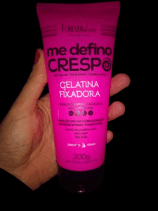 Gelatina Fixafora Forever Liss sendo segurado por uma mão em fundo preto